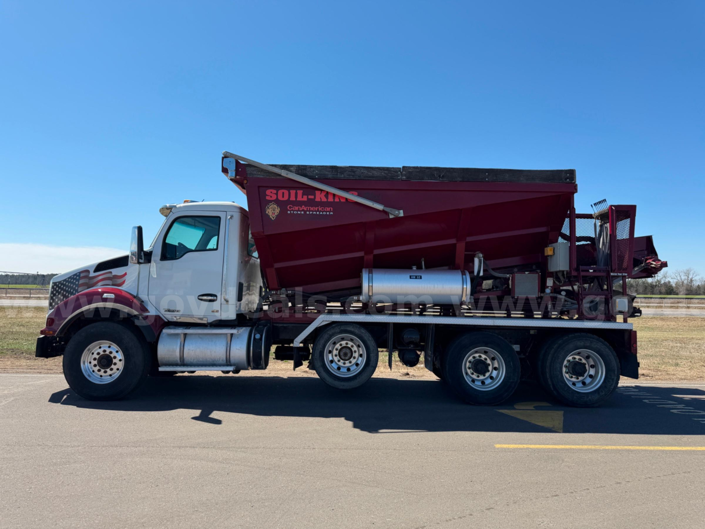 Kenworth T880 dump truck side view showing heavy-duty dual rear axles, dump bed, and fuel tanks. Clear sky, asphalt surface.