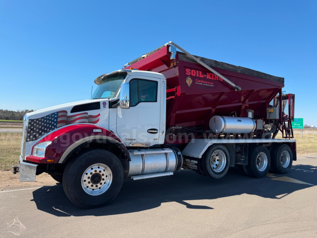 Kenworth T880 dump truck in-service showing large maroon dump body mounted on white tractor with American flag graphic on door, dual rear axles, side tanks.