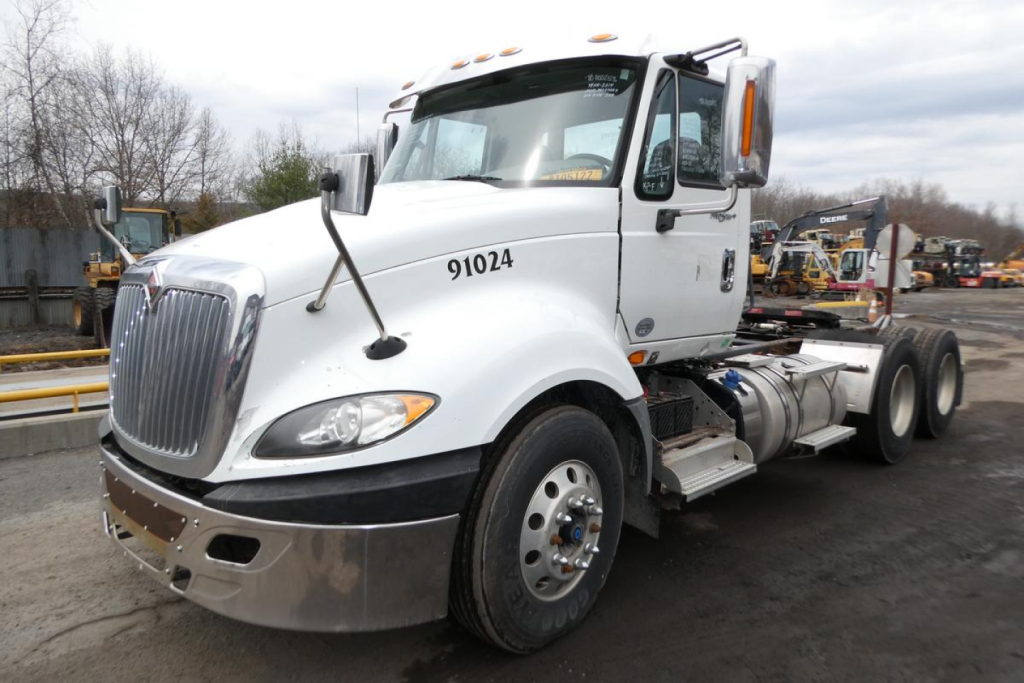 Truck cab and chassis of a white 2014 International PROSTAR+ Daycab showing front grille, headlights, and dual rear axle configuration.
