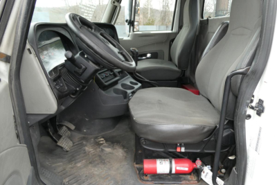 Truck cab interior showing steering wheel, driver's seat, and passenger seat with floor mat and fire extinguisher under seat.