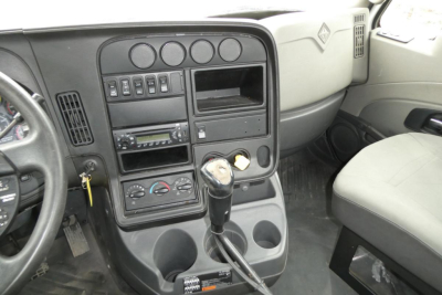 Dashboard view of a truck cab showing steering wheel, instrument cluster, center console with climate controls, radio, empty cup holders, and gear shifter.