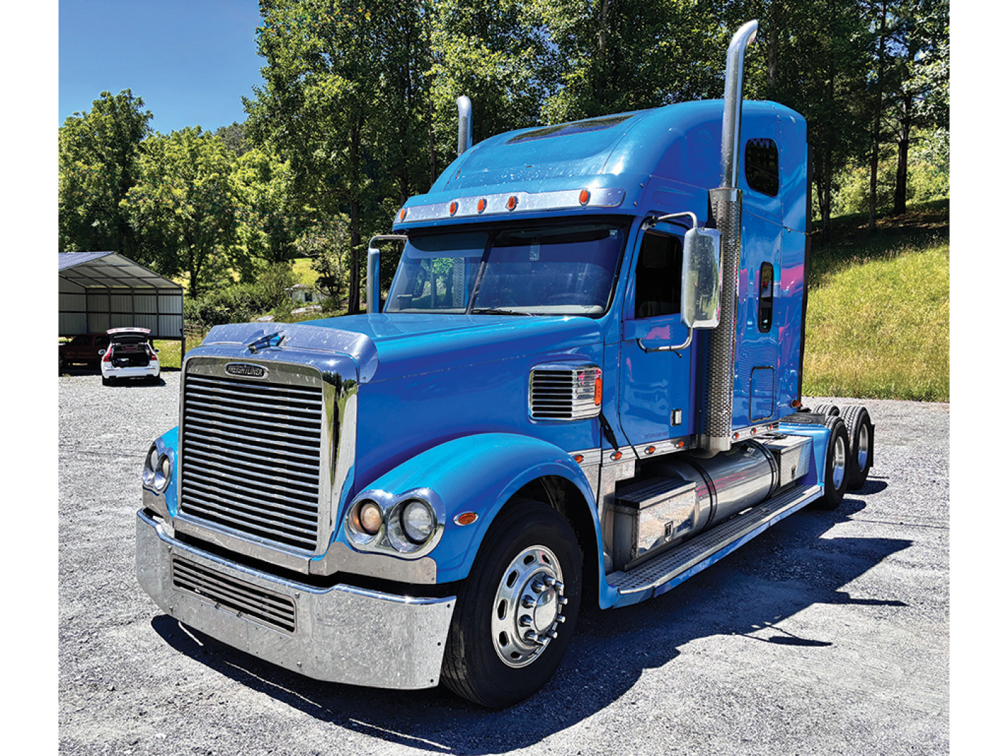Blue Freightliner Coronado truck in-service with high sleeper cab, front grille, chrome bumper, dual stacks, side fuel tanks.