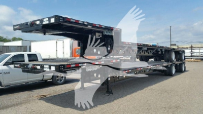 Manac steel drop deck trailer on a lowboy with folded ramp, black frame, dual rear axles, and support legs visible.