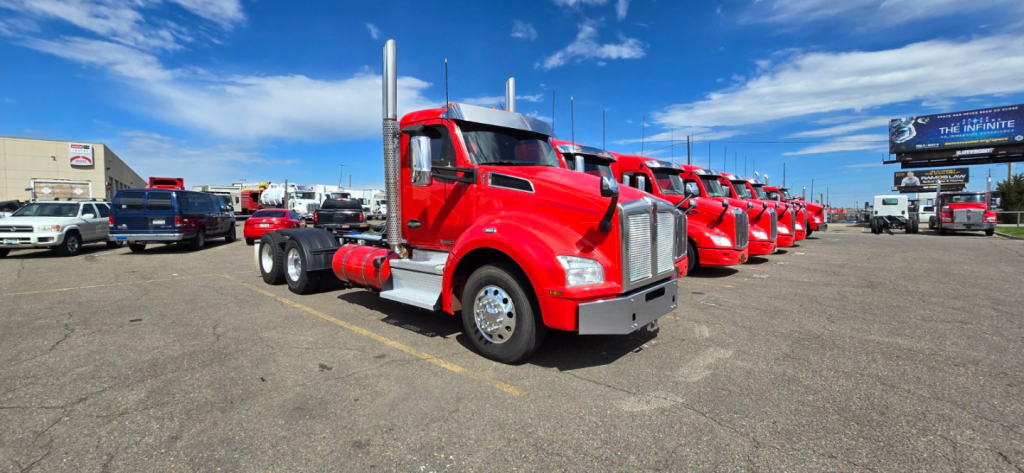 Kenworth T880 conventional daycab trucks in a dealer lot, red color, aligned in a row with blue sky.