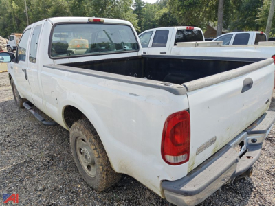 2005 Ford F-250 Super Duty extended cab pickup truck with long bed, white paint, rear view showing tailgate and bed, wheel well dirt, gravel lot.