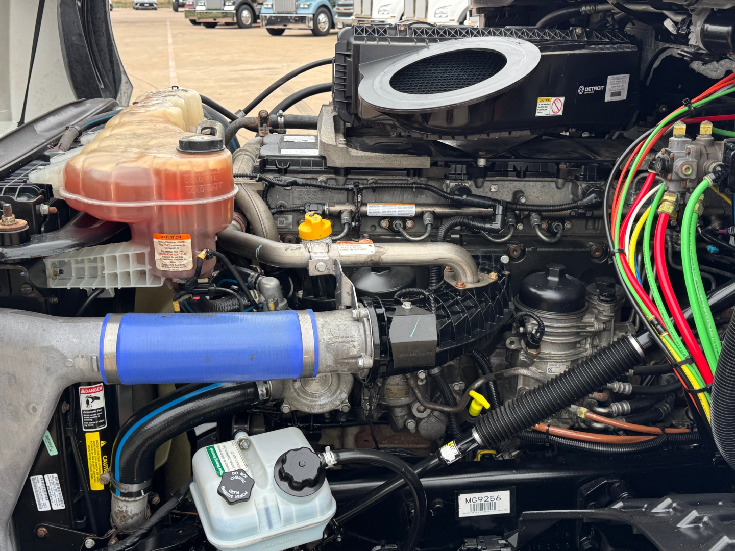 Engine bay of a Freightliner truck with visible coolant reservoir, blue hose, yellow oil dipstick, and wiring harnesses.