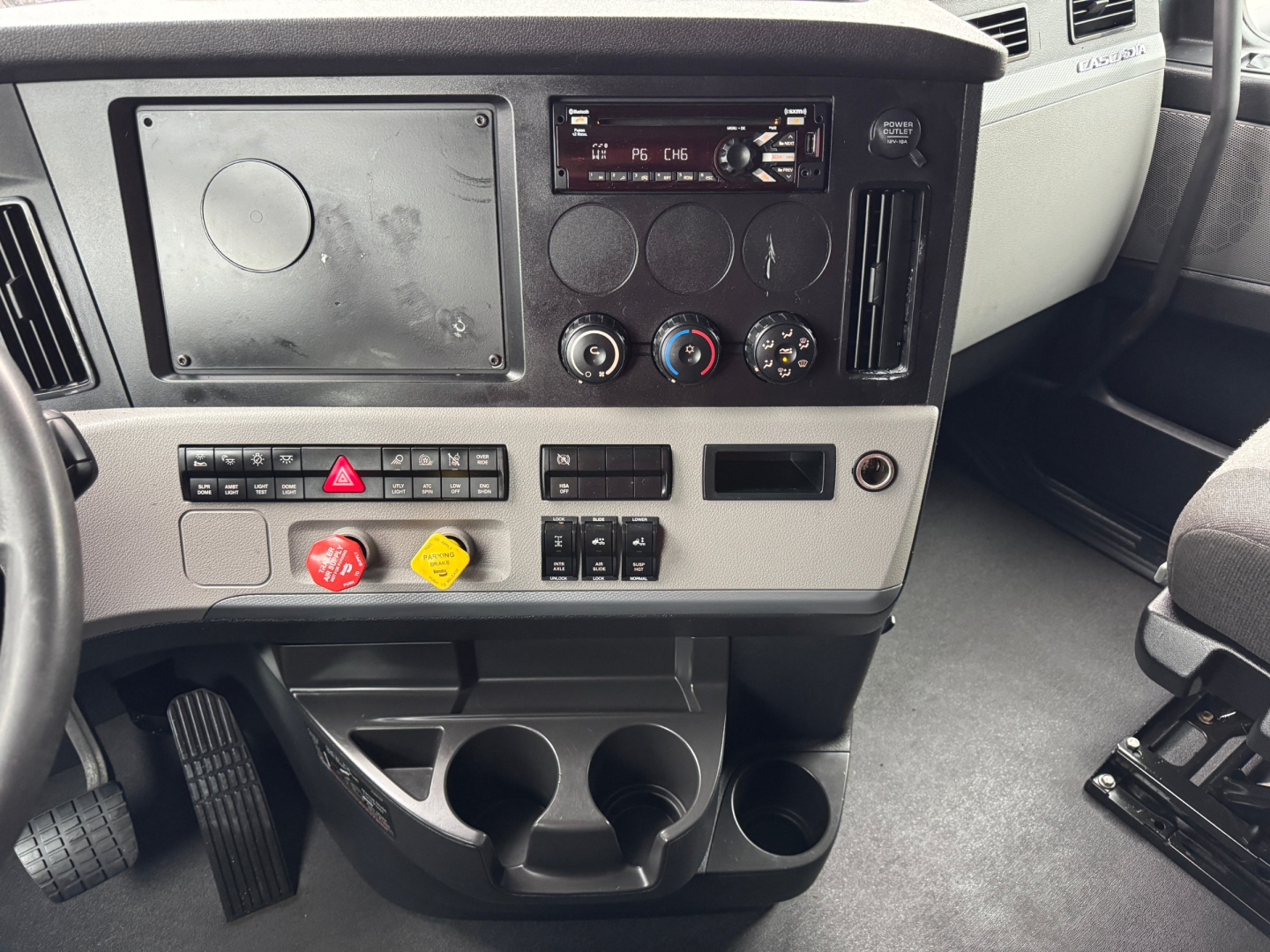 Truck cab dashboard view with controls and cup holders. Visible text includes climate controls, hazard light button, radio, and various switches.