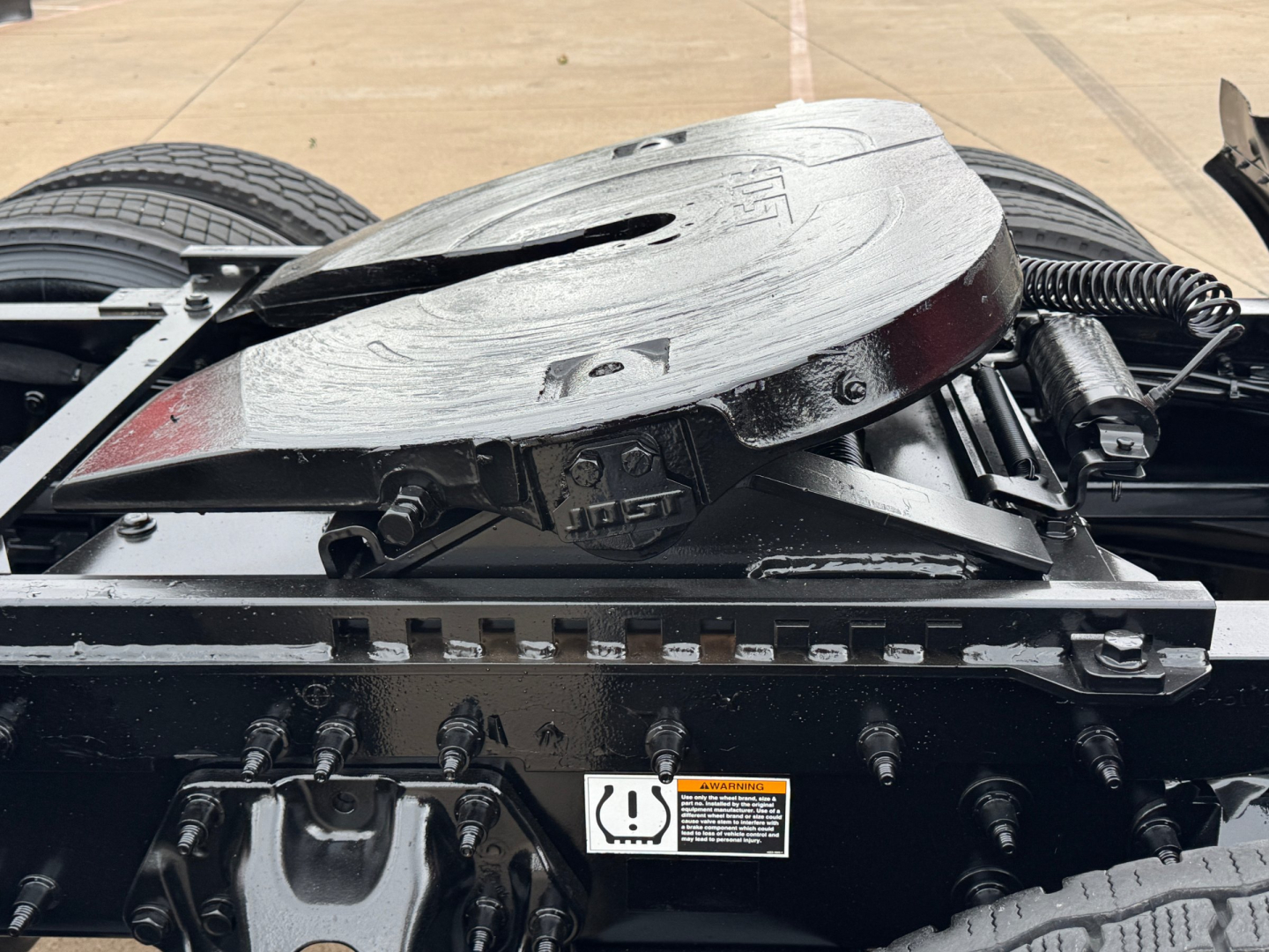 Freightliner drivetrain area showing a circular air reservoir/rotation device and nearby hoses and bolts on a chassis with labels.