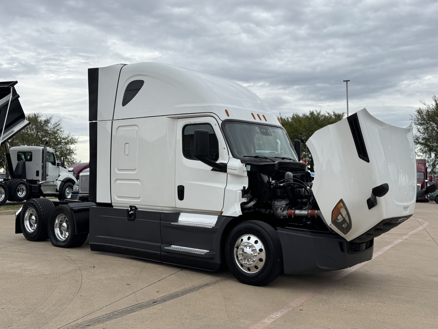 Truck engine bay of a Freightliner tractor with hood open, showing side mirrors, cab, and front wheels.