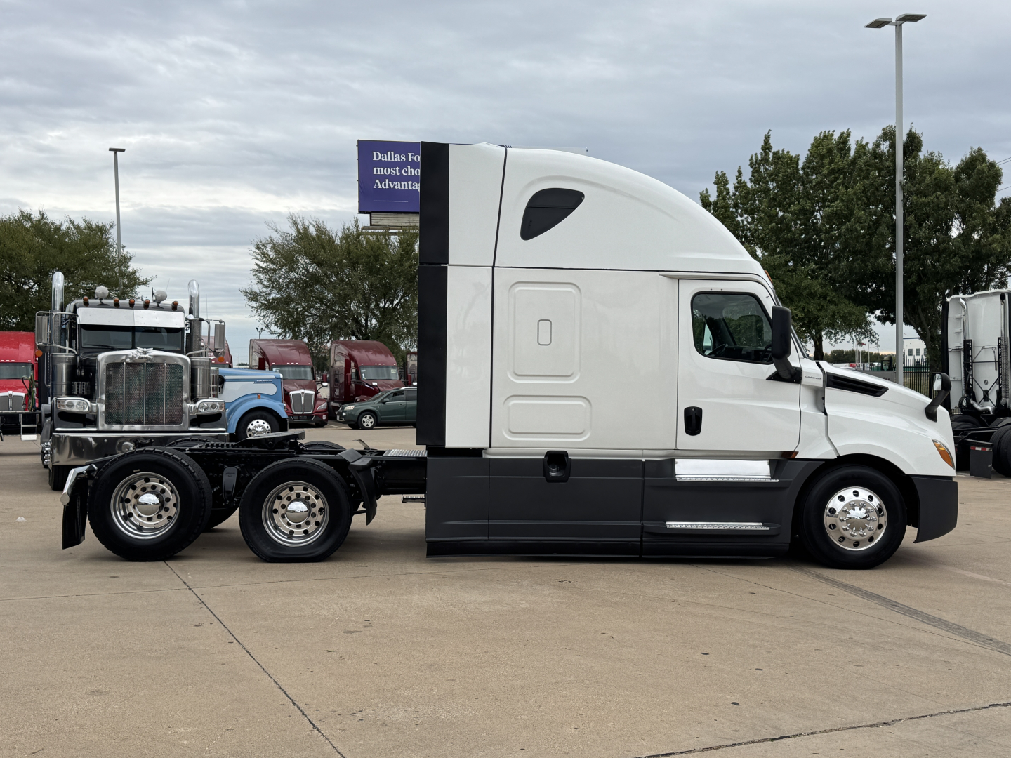 Truck tractor side view showing sleeper cab and six tires on rear axle with white cab and black lower body.