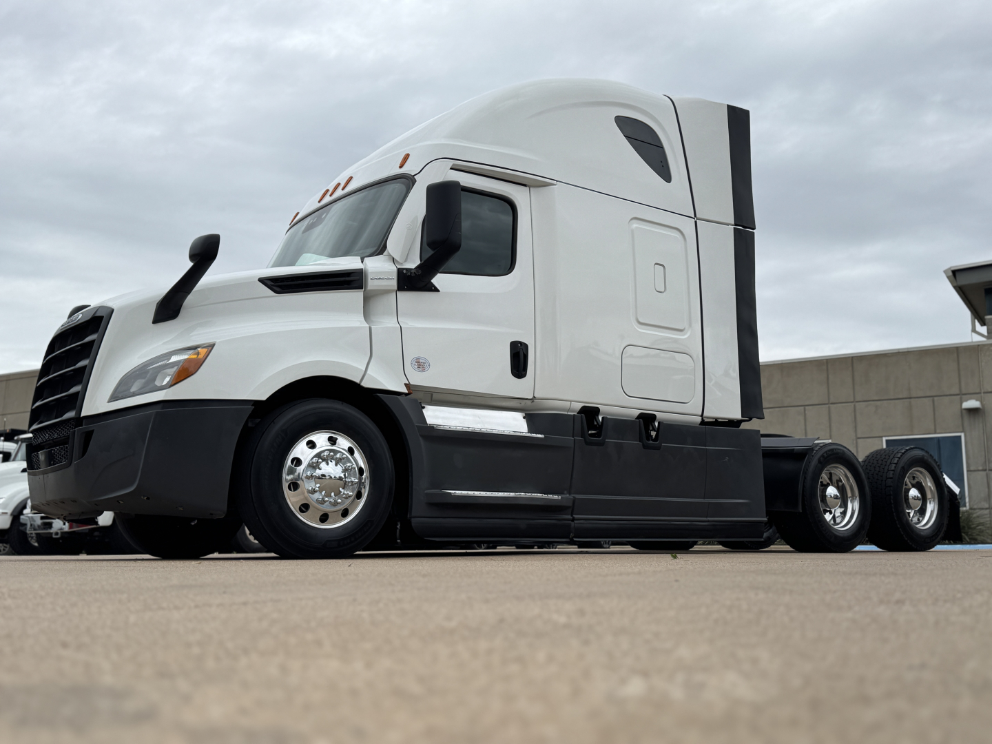 Freightliner semi truck cab in profile view showing aerodynamic white sleeper cab with black lower trim and dual rear axles, stock number 0633000 visible