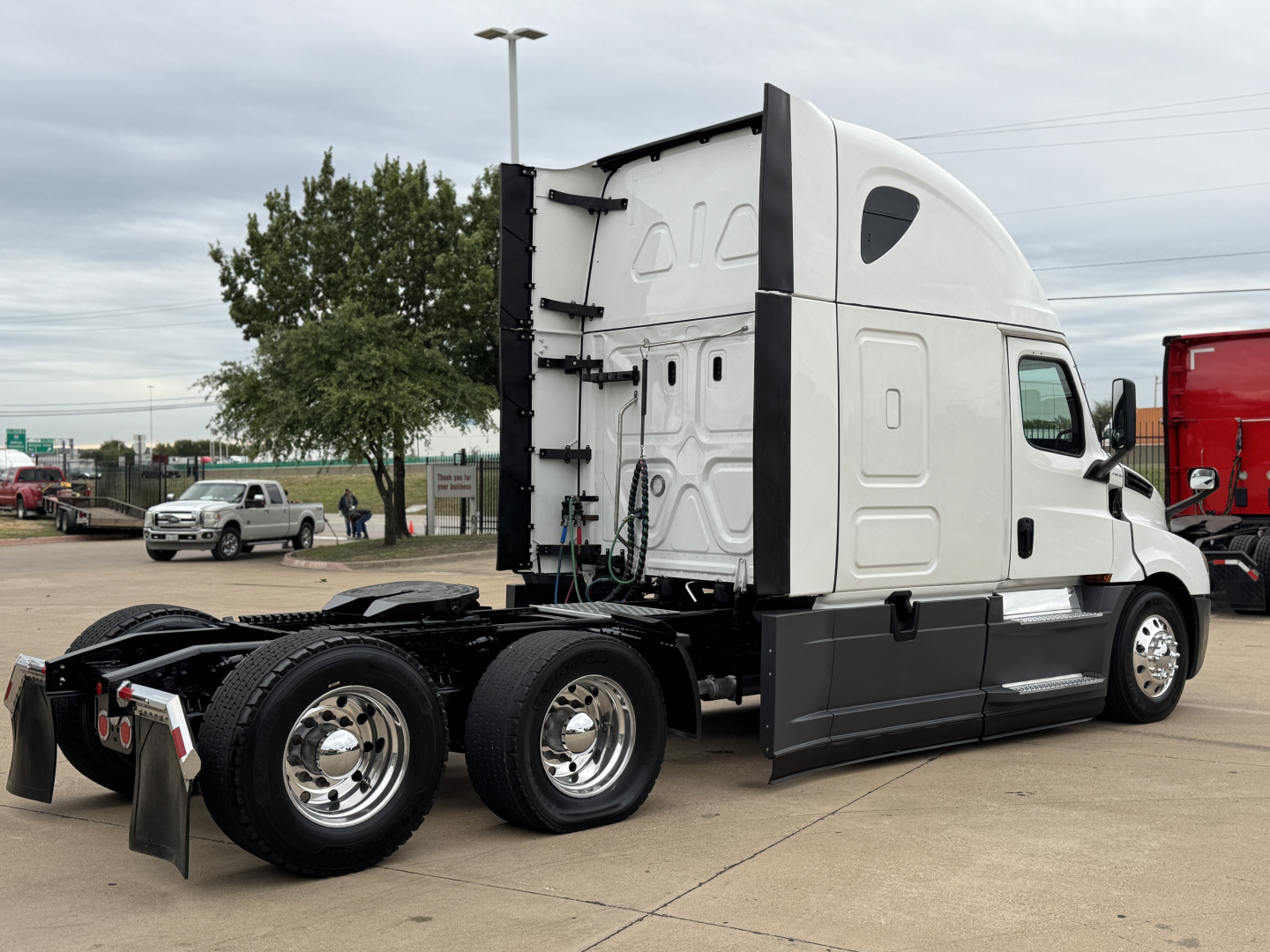 Truck chassis of a Freightliner conventional sleeper with three axles, white cab, black lower panels, and attached rear wheel area with chrome rims.