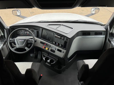 Interior cab view of a Freightliner PT126064ST truck showing dashboard with steering wheel, gauges, control panel, and center console; driver and passenger seats visible.
