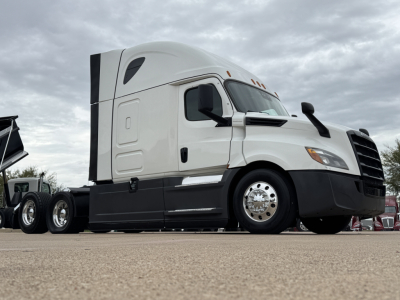 Freightliner cab in clean white with sleeper, side view showing front wheel and chrome hubcap, attached trailer chassis visible.