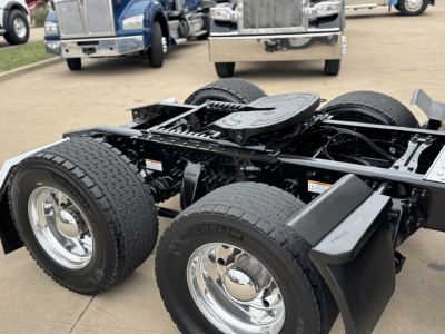 Tractor truck chassis with dual rear axles and dual tires showing chrome wheels, fuel tanks, and frame. Partial cab area visible in background.