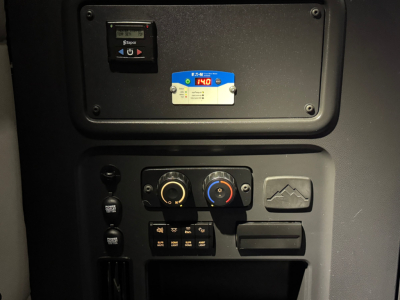 Dashboard panel of Freightliner PT126064ST showing control switches, two round dials, blue and red AC/heat controls, and a small blue badge with numbers.