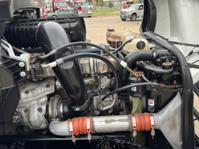 Truck engine bay showing labels and components including hoses, coolant reservoir, and turbo piping; visible text includes no legible serials or brands readable in image.