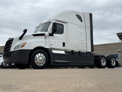 Freightliner semi truck cab in profile view showing aerodynamic white sleeper cab with black lower trim and dual rear axles, stock number 0633000 visible