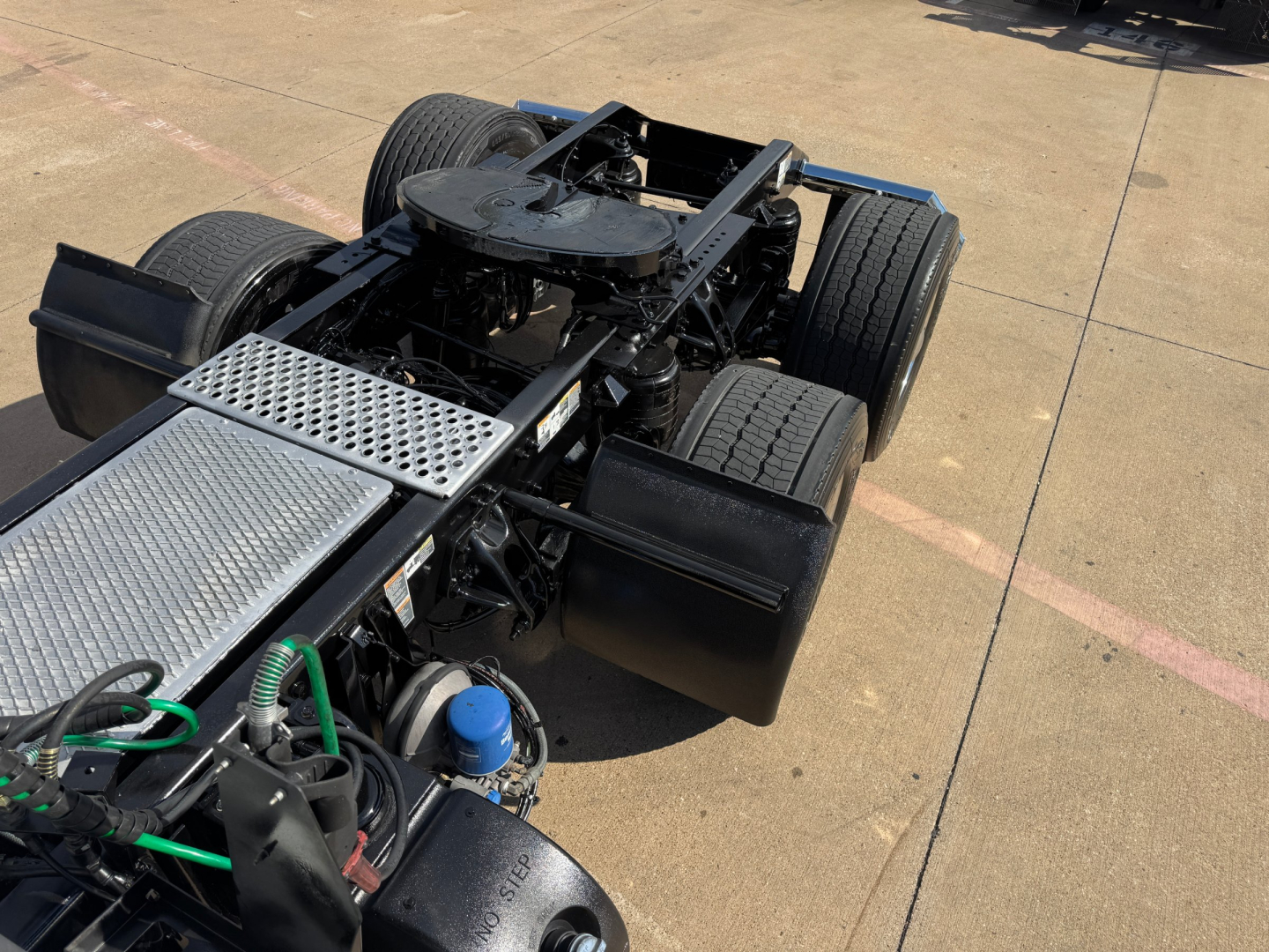 Kenworth truck chassis and cabless rear view showing fifth wheel, dual rear axles, fuel tanks, air lines, and exposed frame with metal diamond plate walkway.