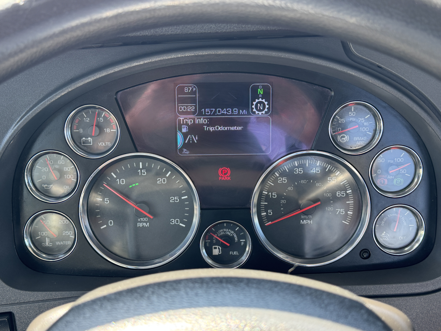 Dashboard of a Kenworth T680 showing multiple gauges and center display with TripInfo and odometer; left and right gauges indicate RPM, speed, fuel, and air pressure.