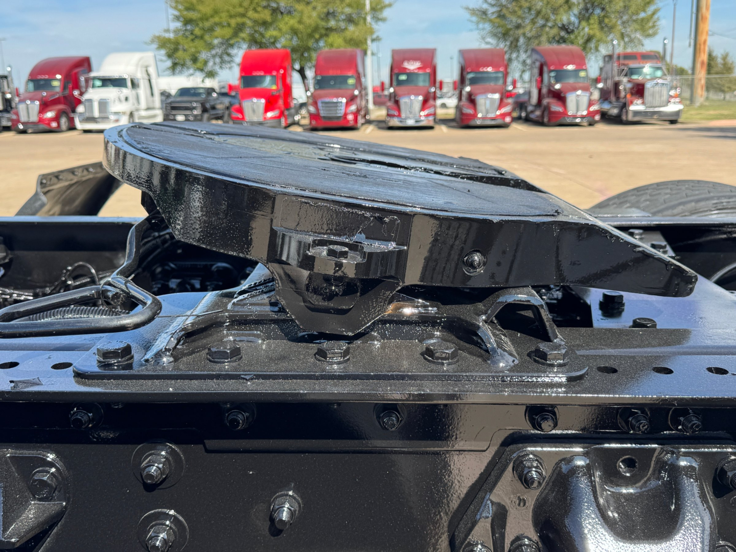 Kenworth T680 tractor trailer: top of fifth wheel coupling and mounting surface, black components, multiple red trucks in background.