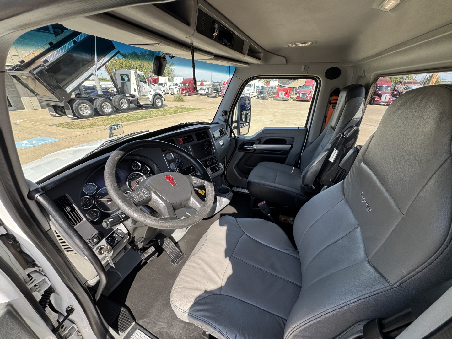 Interior of a Kenworth T680 truck cab showing steering wheel, dashboard, and front seats with visible controls and gauges.