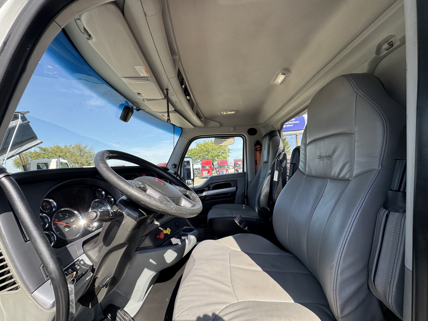 Interior of 2022 Kenworth T680 cab showing steering wheel, dashboard, and driver seat with light gray upholstery.