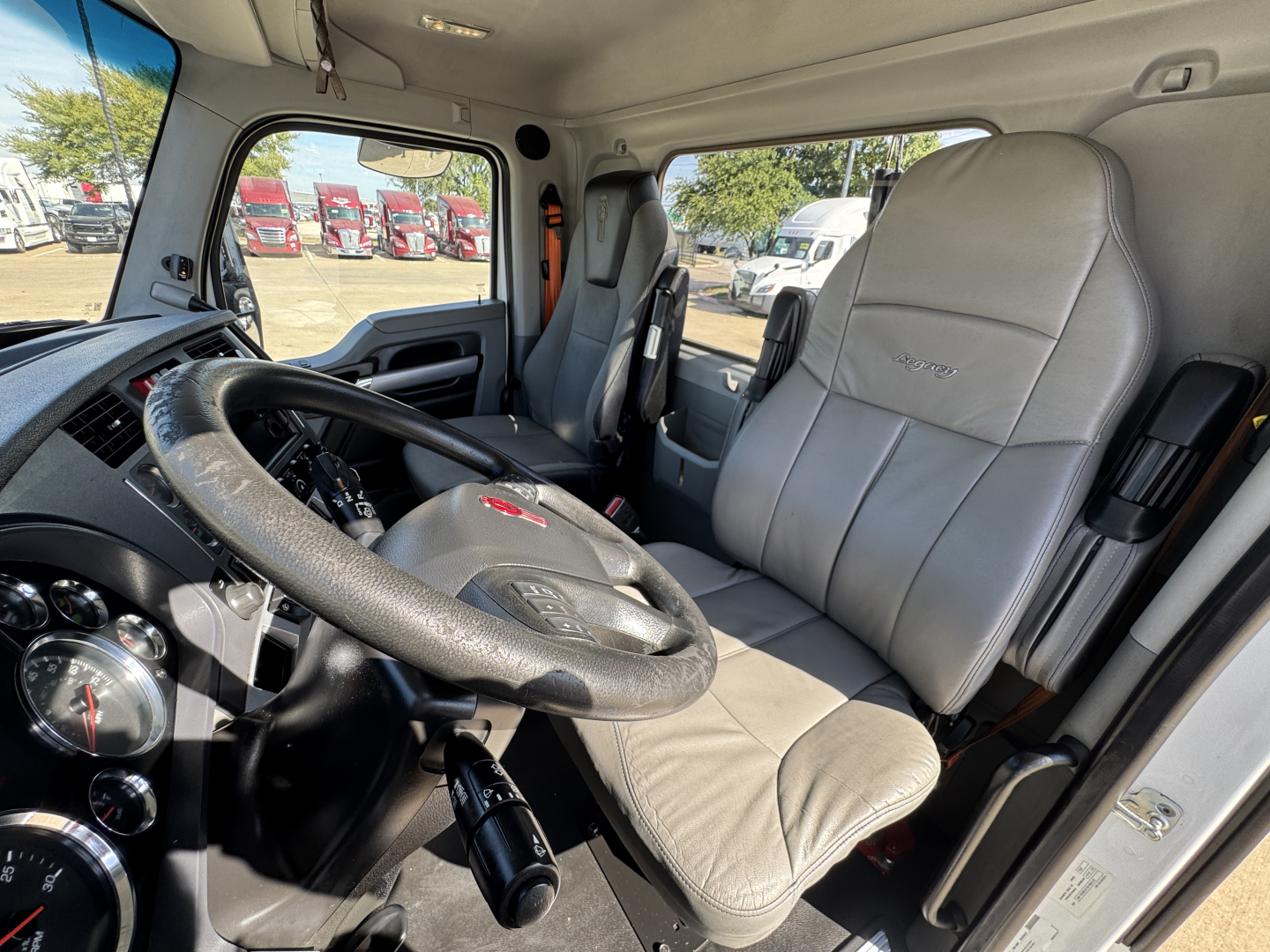 Kenworth T680 interior showing steering wheel, driver seat, and dashboard in view with gray upholstery.
