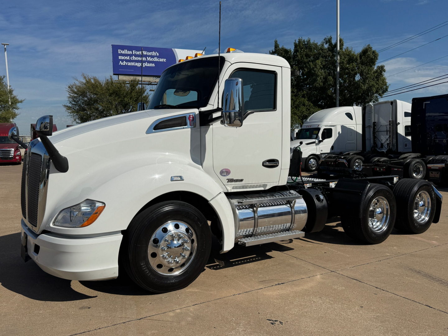 Kenworth T680 tractor cab in white, side view showing chrome fuel tanks and dual rear axles.