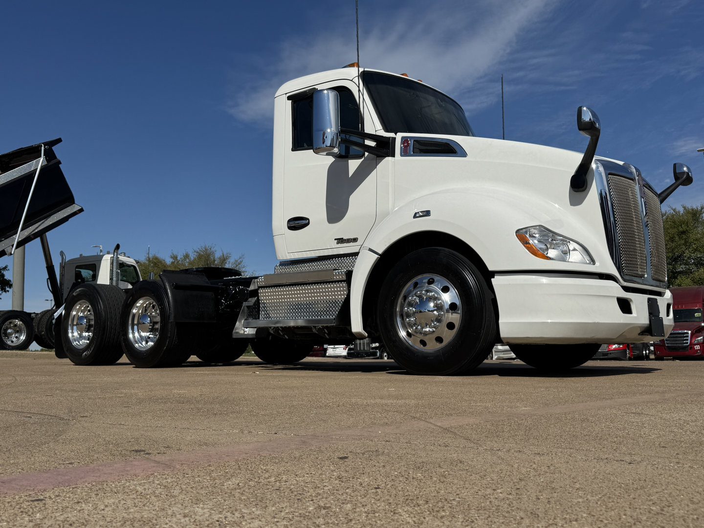 Kenworth T680 conventional daycab truck in-profile with white cab, chrome wheels, and dual fuel tanks; visible text on truck includes Kenworth badge and side mirrors; no additional readable labels or numbers visible.