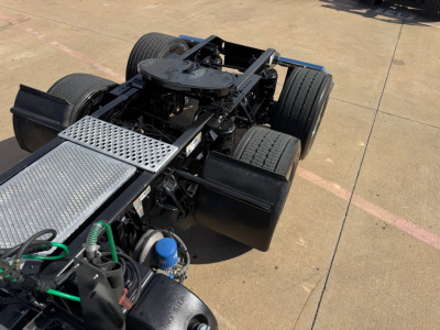 Kenworth truck chassis and cabless rear view showing fifth wheel, dual rear axles, fuel tanks, air lines, and exposed frame with metal diamond plate walkway.