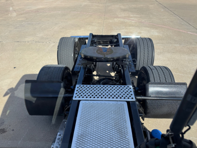 Kenworth truck chassis view from rear showing cab-less frame and fifth wheel mounting with dual rear axles and toolbox; metal diamond plate steps visible.