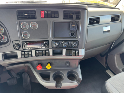 Kenworth T680 dash and gauge cluster showing steering wheel area and center console with switches, ignition, and two cup holders.