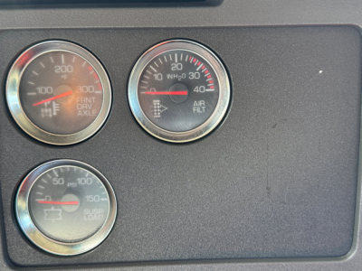 Trucks dashboard gauges showing RPM/FRNT AXLE, AIR FILT, SUSP/LOAD with needles at mid ranges.