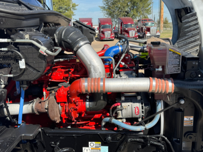 Kenworth T680 engine bay showing red engine block and gray turbo pipe with orange ribbed couplers and various blue hoses.