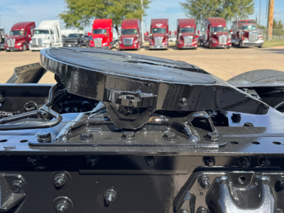 Kenworth T680 tractor trailer: top of fifth wheel coupling and mounting surface, black components, multiple red trucks in background.