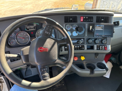 Kenworth T680 cockpit showing steering wheel with red Kenworth logo, instrument cluster, dashboard switches, gauges, and center touchscreen.