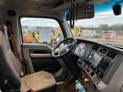 Kenworth T680 driver cabin interior showing steering wheel, dashboard with control panel, seat, and windshield with some equipment outside.