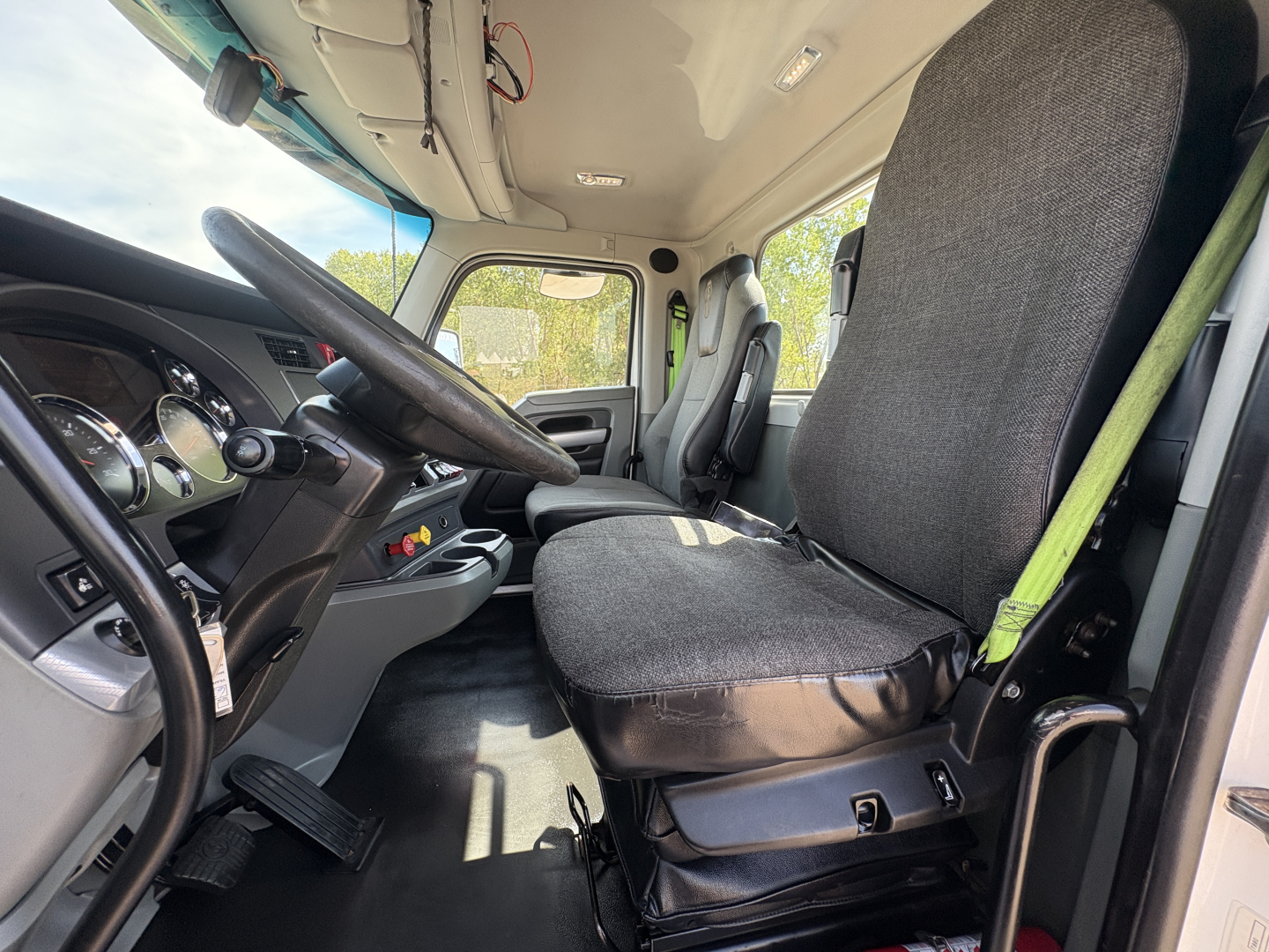Truck cab interior showing steering wheel, dashboard, and driver seat in a Kenworth T880 cab. No visible text on components; interior features include instrument cluster, pedals, and seat belts.