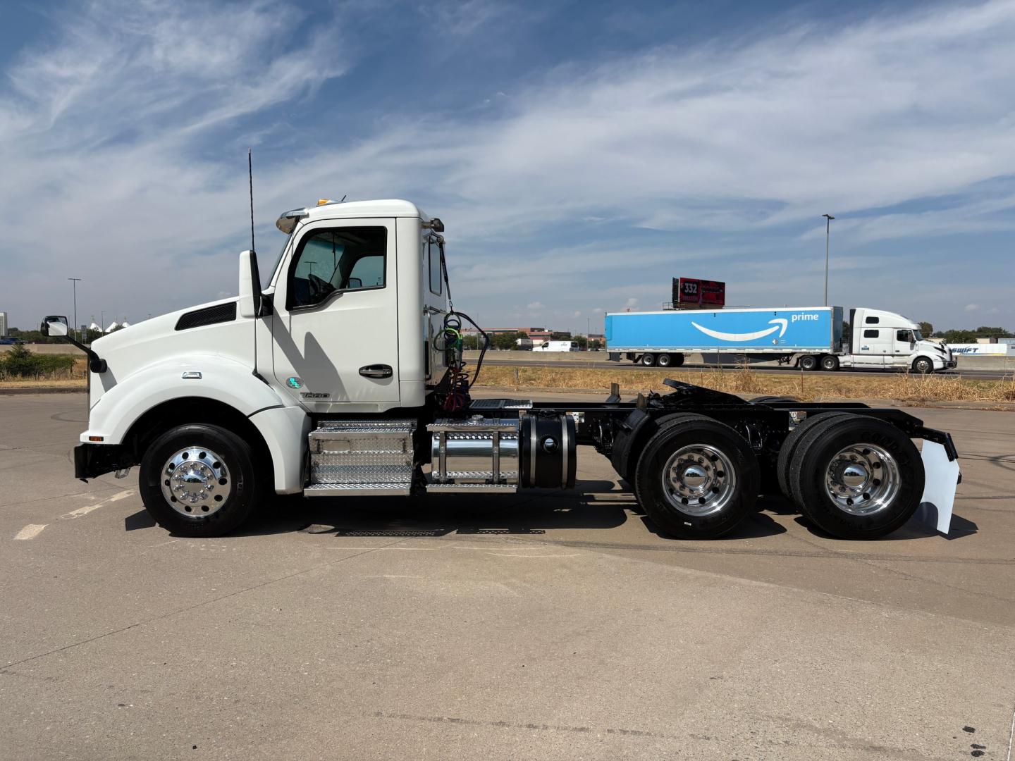 Kenworth T880 daycab truck side view showing chassis, fuel tanks, and triple rear axles with white cab and black tires.