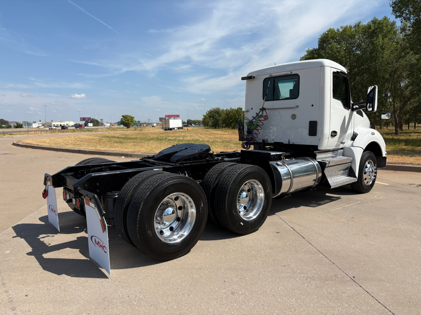 Kenworth T880 tractor side view showing a white cab and dual rear axles with chrome fuel tanks; no visible text other than reflective mudflaps.