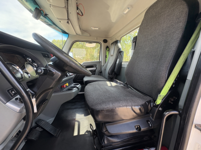 Truck cab interior showing steering wheel, dashboard, and driver seat in a Kenworth T880 cab. No visible text on components; interior features include instrument cluster, pedals, and seat belts.
