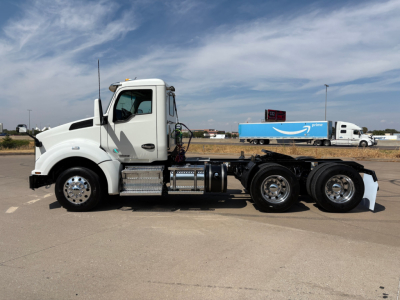 Kenworth T880 daycab truck side view showing chassis, fuel tanks, and triple rear axles with white cab and black tires.