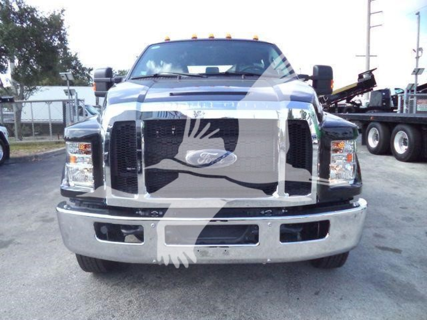 Front view of a Ford F-750 rollback truck showing chrome grille, bumper, and emblem; highway-lander with clearance lights on cab roof.