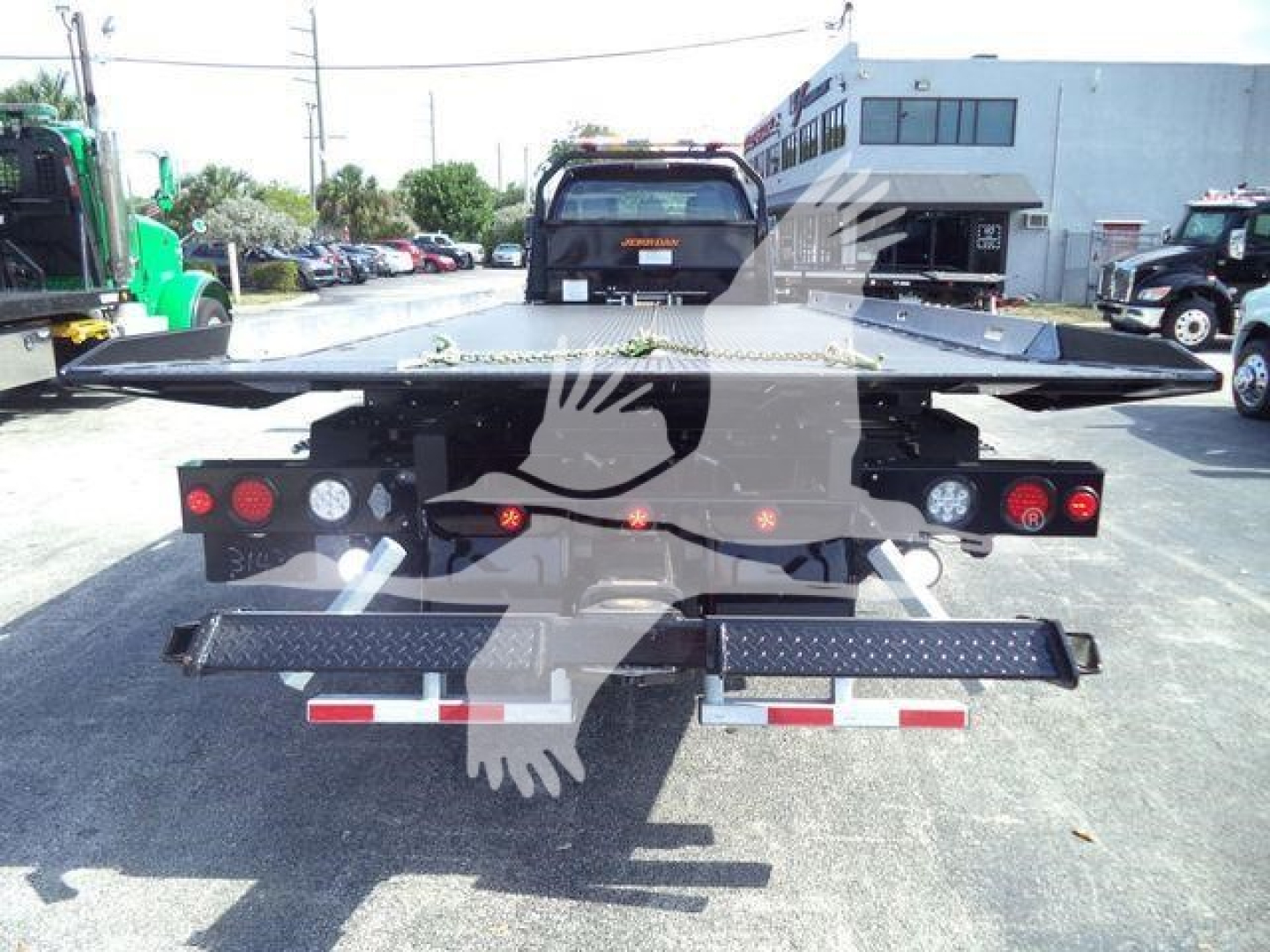 Rear view of a 2025 Ford F750 rollback wrecker chassis showing a flat bed and rear lights, with a dealership lot in the background.