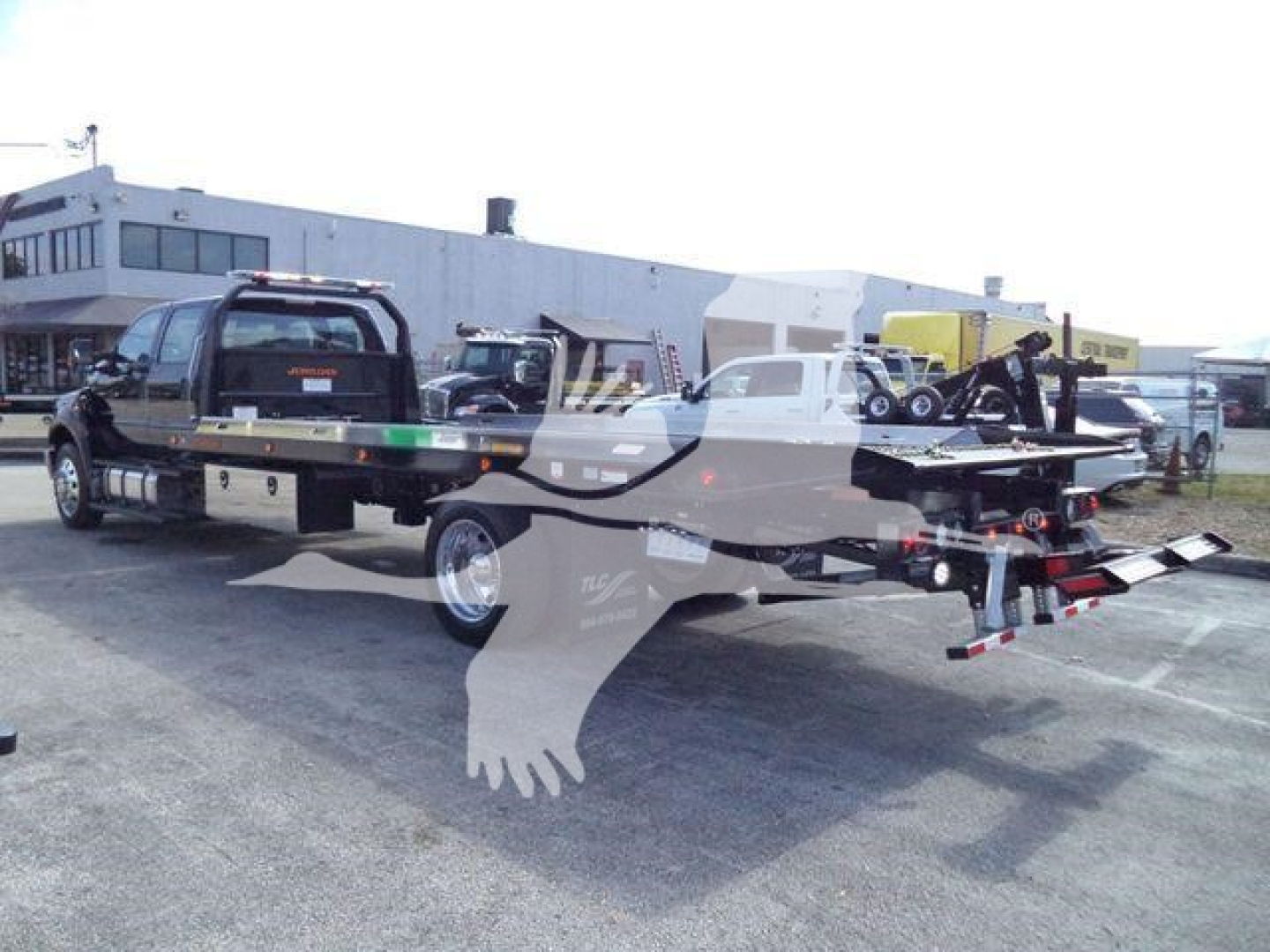 Ford F-750 truck with rollback bed and tow equipment, viewed from side in an outdoor lot.