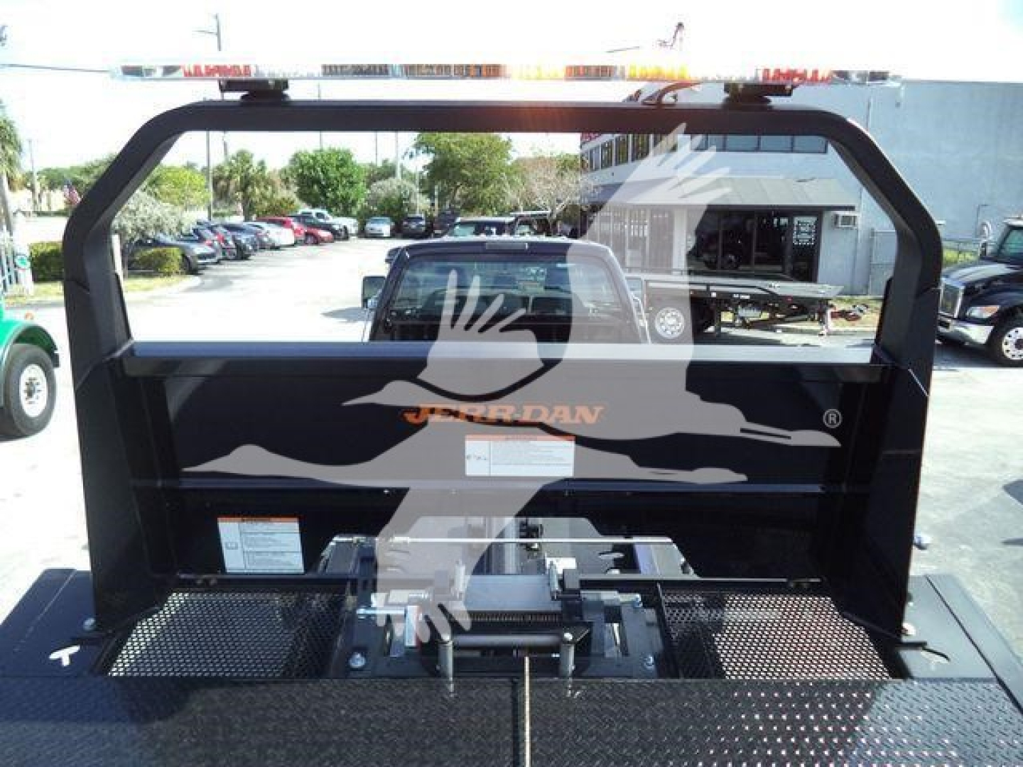 Truck bed with hydraulic rollback equipment and heavy-duty frame, rear view showing label and control components.