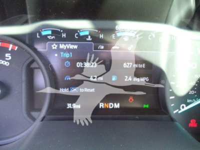Dashboard display of a 2025 Ford F750 XLT showing trip data: Trip 1, 01:38:23, 627 mi to E, 4.2 mi, 2.4 avg MPG, RNDM gear indicator, hold OK to reset, warning icons.