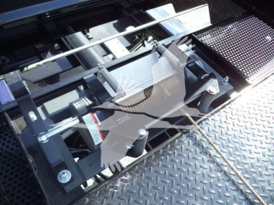 Trucks equipment photo showing hydraulic boom/strut system and cable on a platform likely for a rollback tow truck. Visible components include metal rails, bolts, and a textured diamond plate surface.