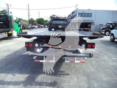 Flatbed tow truck rear with loading ramps and lights, Ford F750 XLT SD label visible on back, in a dealership lot.